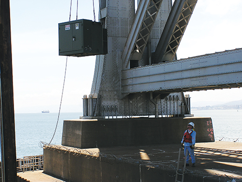 Photo 3. Landing the last medium voltage transformer at the base of the existing SFO Bay Bridge (E2) for temporary construction power. The challenge here was coordination with the tugboats, barge, crane operator and pile bucks.